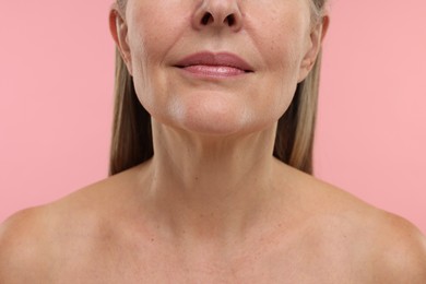 Mature woman showing her neck on pink background, closeup