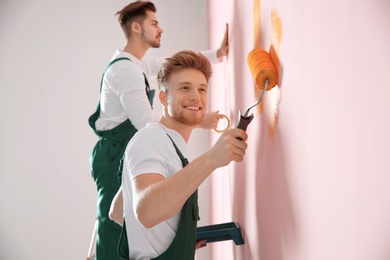 Photo of Professional decorators painting wall indoors. Home repair service