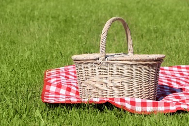 Photo of Picnic basket with checkered tablecloth on green grass outdoors, space for text