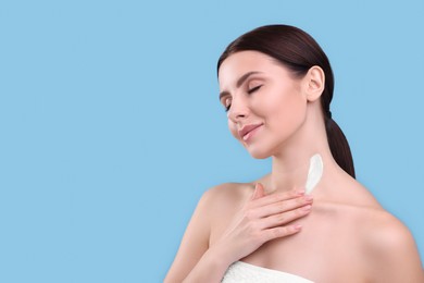 Photo of Beautiful woman with smear of body cream on her neck against light blue background, space for text