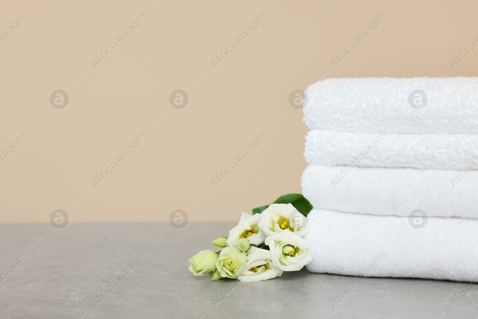 Photo of Soft folded towels and eustoma flowers on grey table, space for text