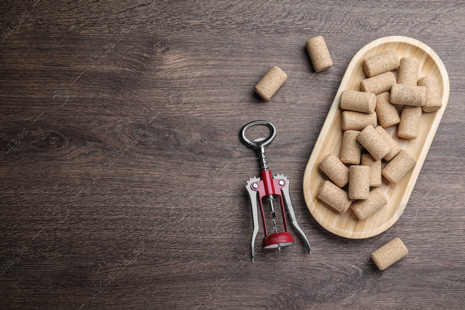 Photo of Corkscrew and wine bottle stoppers with plate on wooden table, flat lay. Space for text