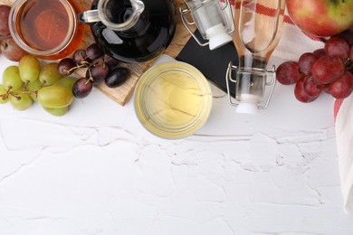 Different types of vinegar and fresh fruits on white table, top view. Space for text