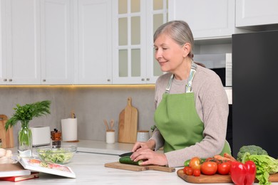 Photo of Senior woman cooking by recipe book in kitchen