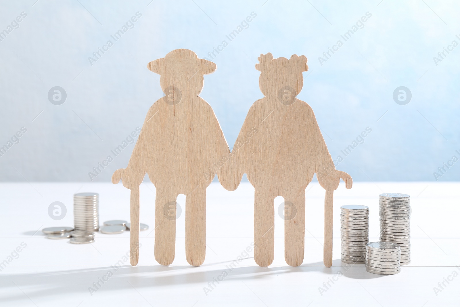 Photo of Pension savings. Figure of senior couple and coins on white wooden table