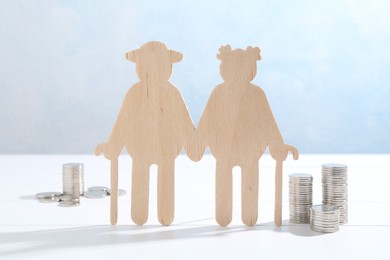 Pension savings. Figure of senior couple and coins on white wooden table