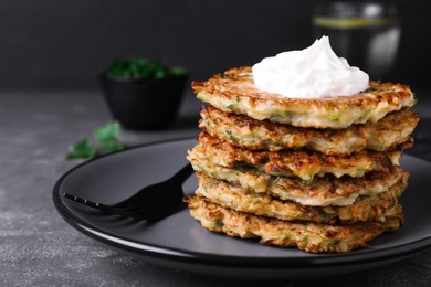 Photo of Delicious zucchini fritters with sour cream on grey table, closeup. Space for text