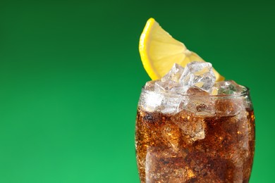 Photo of Glass of refreshing soda drink with ice cubes and lemon on green background, closeup. Space for text