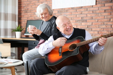 Photo of Elderly man playing guitar for his wife on sofa in living room