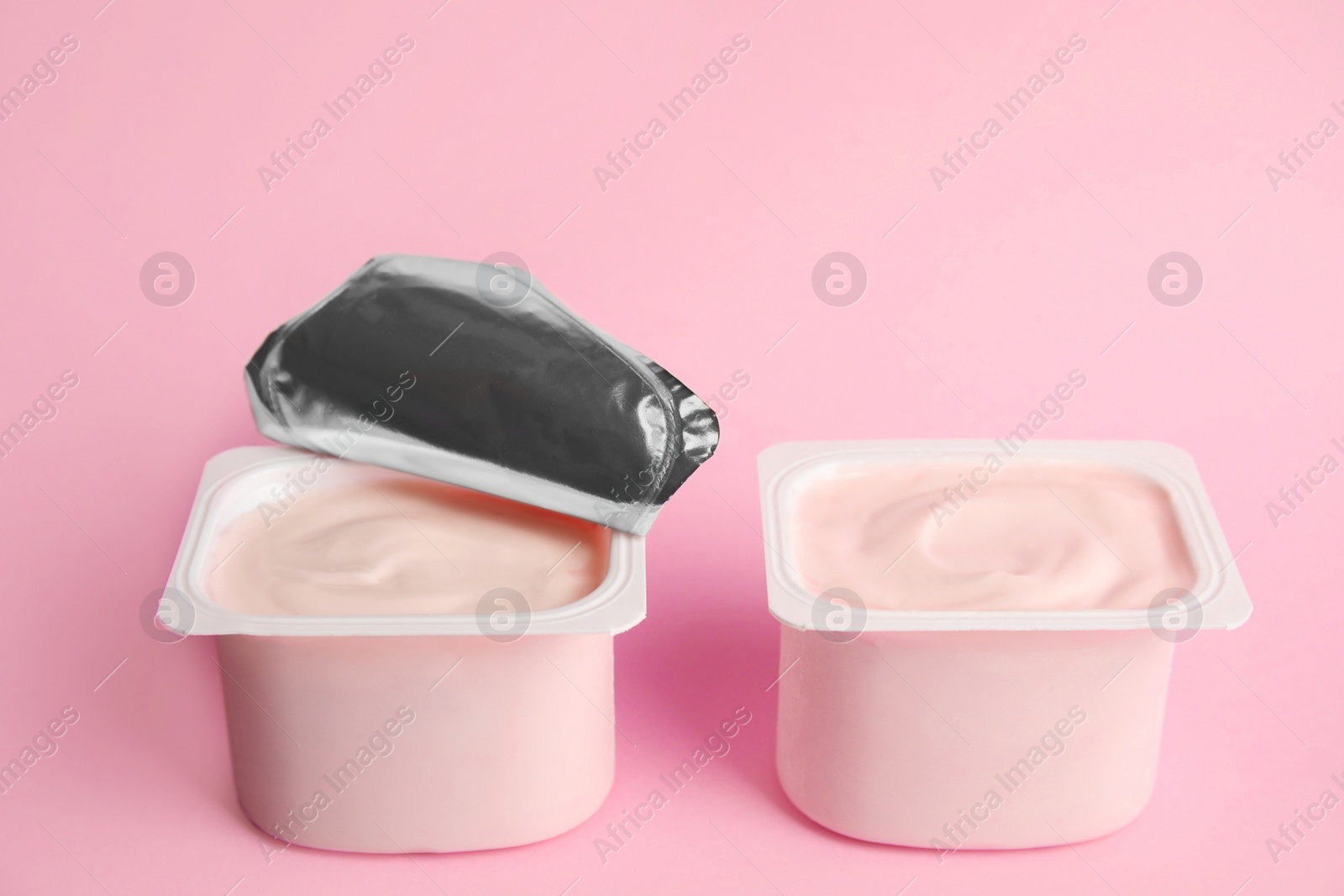 Photo of Tasty organic yogurt in plastic cups on pink background