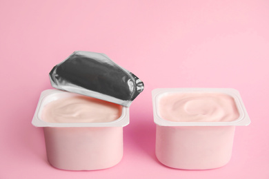 Tasty organic yogurt in plastic cups on pink background