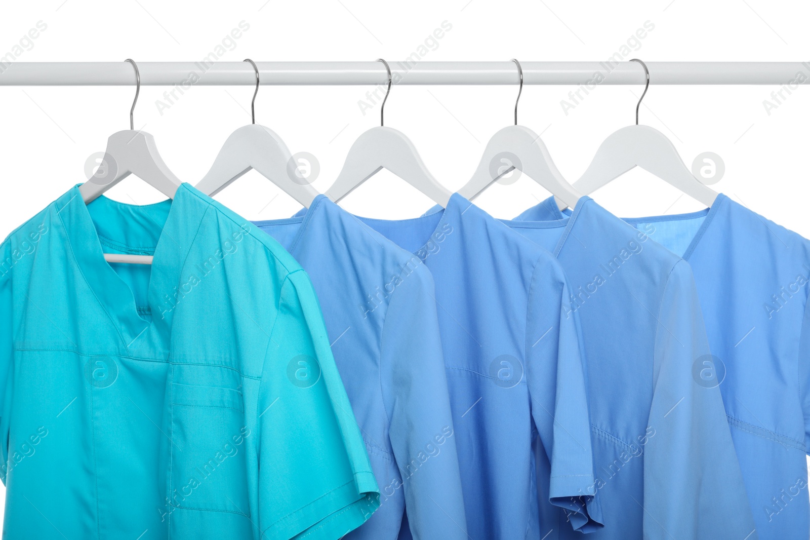 Photo of Turquoise and light blue medical uniforms on rack against white background