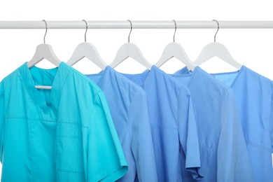 Photo of Turquoise and light blue medical uniforms on rack against white background