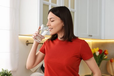 Photo of Young woman drinking fresh water in kitchen