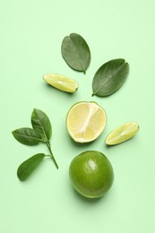 Photo of Whole and cut fresh ripe limes with leaves on light green background, flat lay