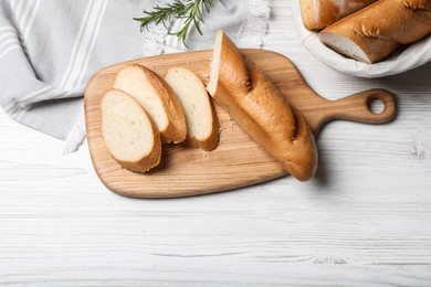 Photo of Cut tasty baguette with rosemary on white wooden table, flat lay