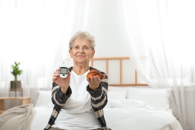 Photo of Senior woman holding digital glucometer and pastry at home. Diabetes diet