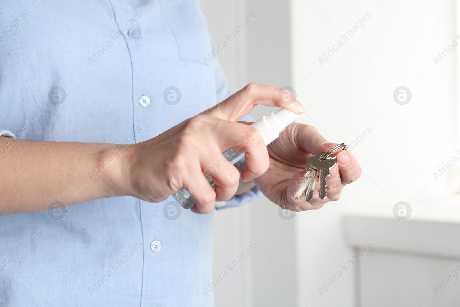 Photo of Woman spraying antiseptic onto keys indoors, closeup