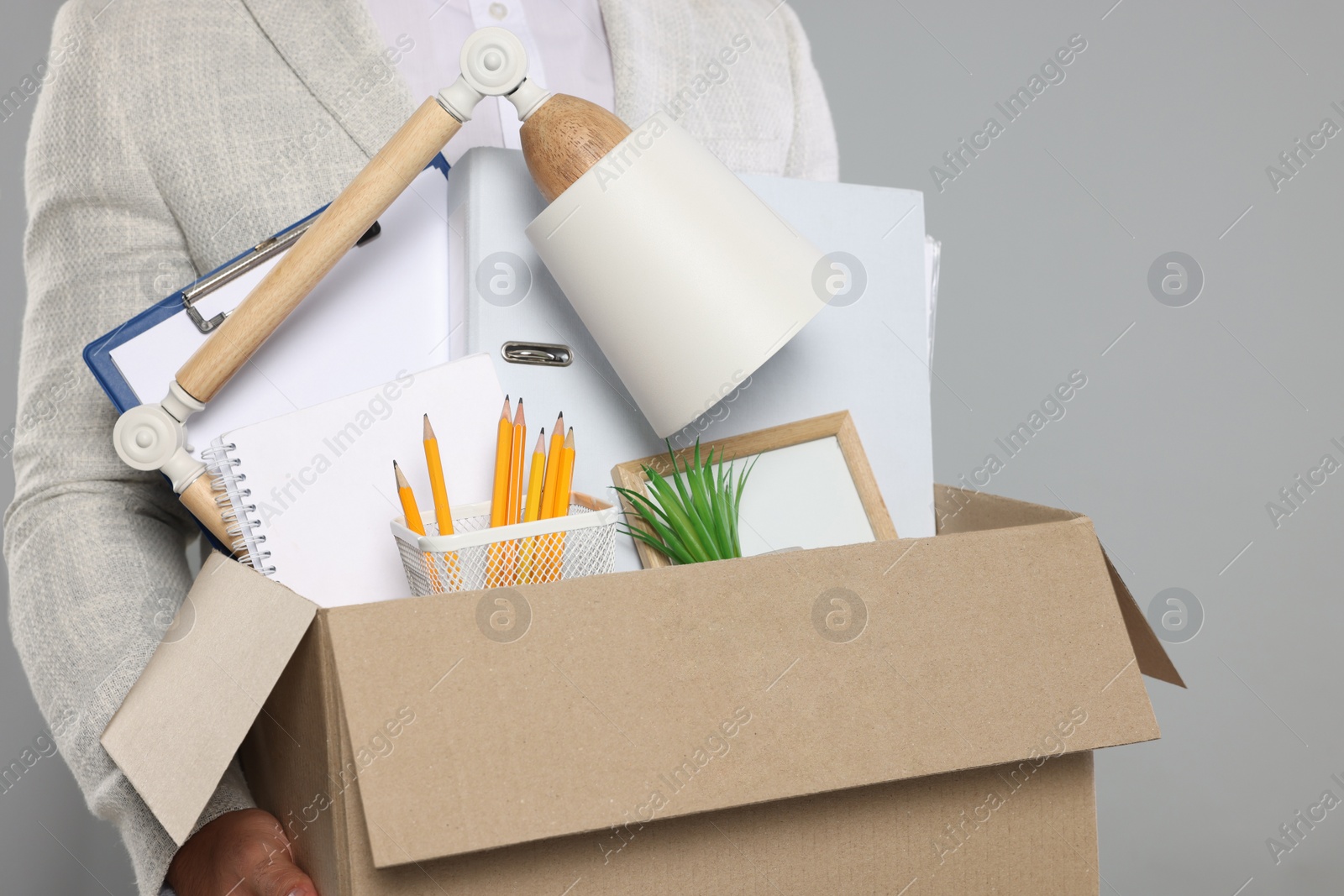 Photo of Unemployed man with box of personal office belongings on light grey background, closeup