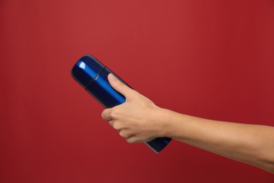 Woman holding modern blue thermos on red background, closeup