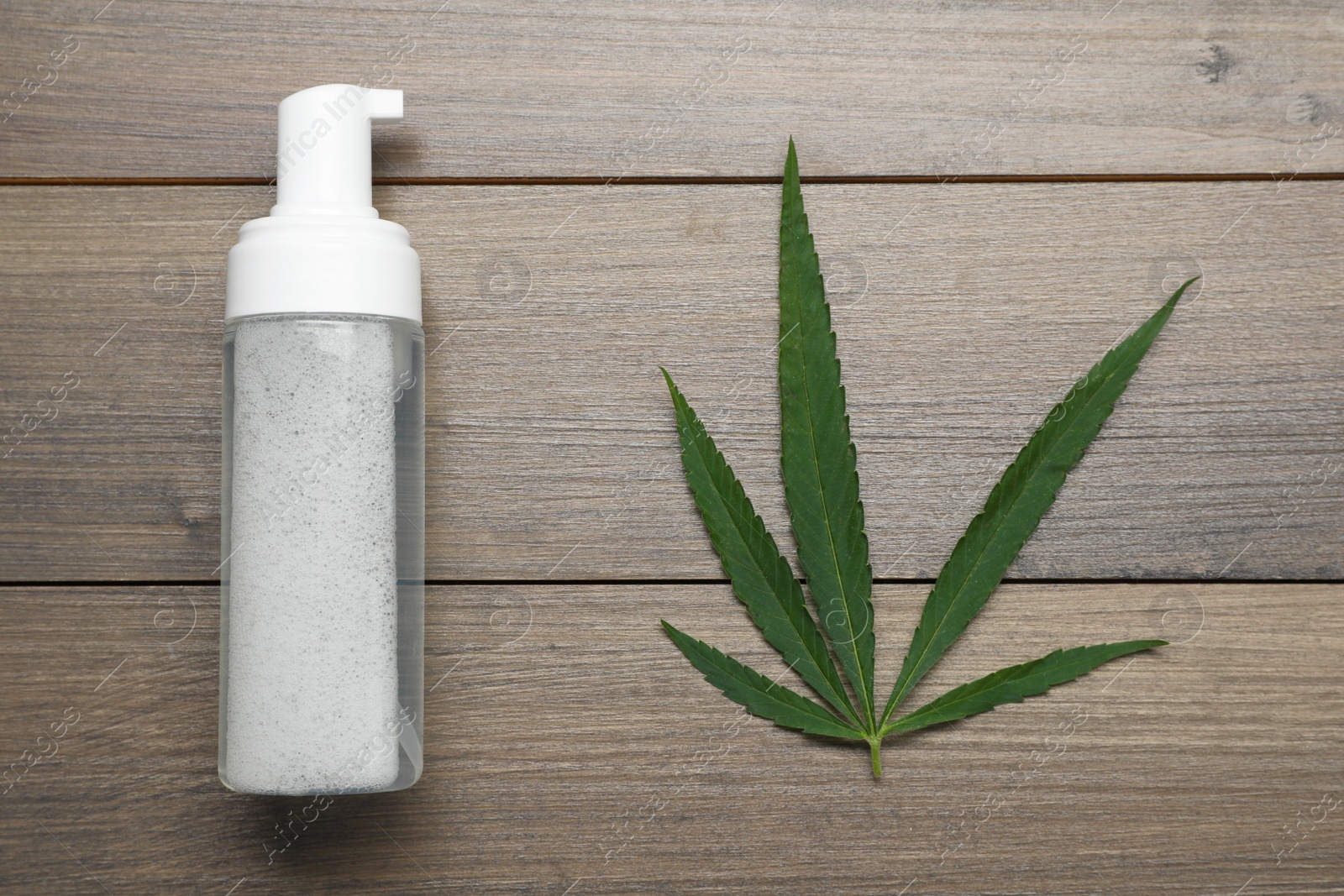 Photo of Bottle of hemp cosmetics and green leaf on wooden table, flat lay