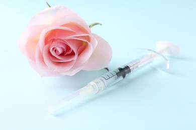Photo of Cosmetology. Medical syringe and rose flower on light blue background, closeup