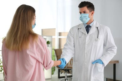 Photo of Doctor and patient in protective masks shaking hands indoors