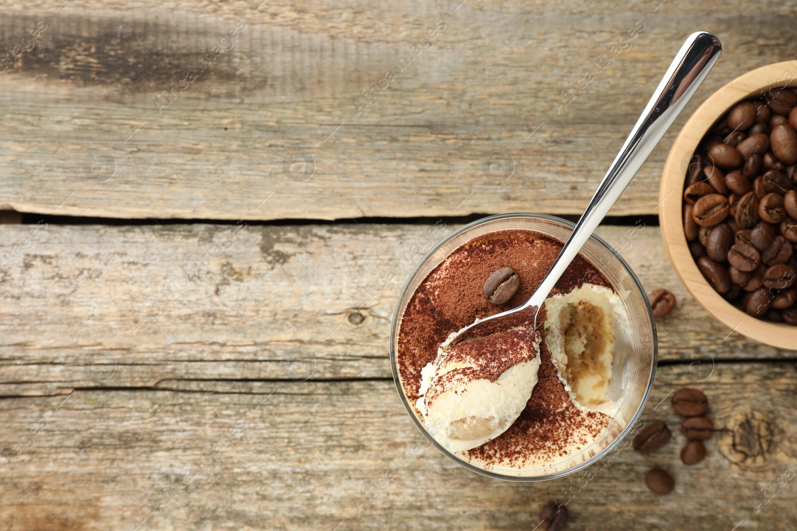 Photo of Delicious tiramisu in glass, spoon and coffee beans on wooden table, top view. Space for text