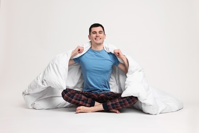 Happy man in pyjama wrapped in blanket on light grey background