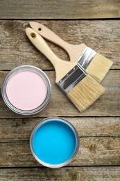 Photo of Cans of colorful paints and brushes on wooden table, flat lay