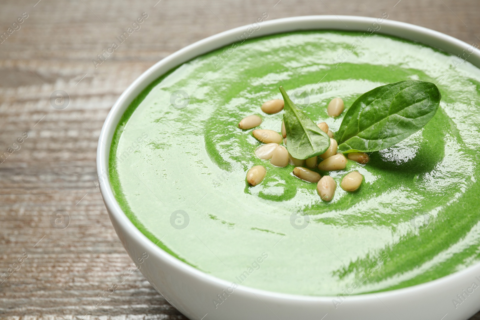 Photo of Bowl of healthy green soup with fresh spinach on wooden table, closeup view