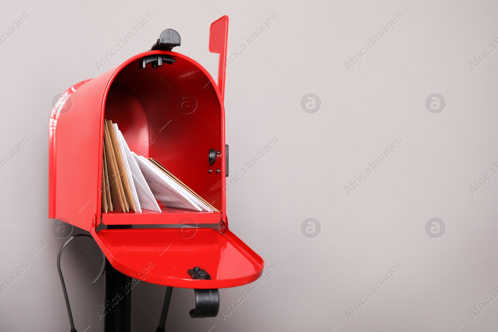 Photo of Open red letter box with envelopes against grey background. Space for text