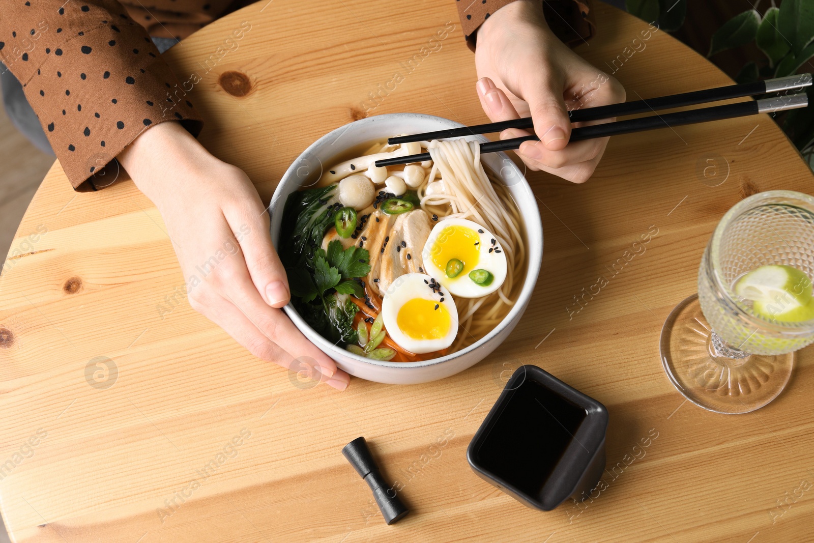 Photo of Woman eating delicious ramen with chopsticks at wooden table, above view. Noodle soup