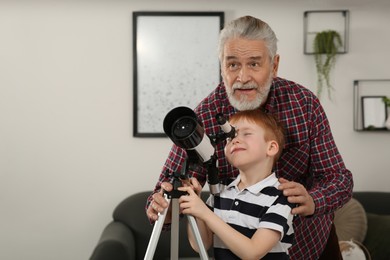 Little boy with his grandfather looking at stars through telescope in room