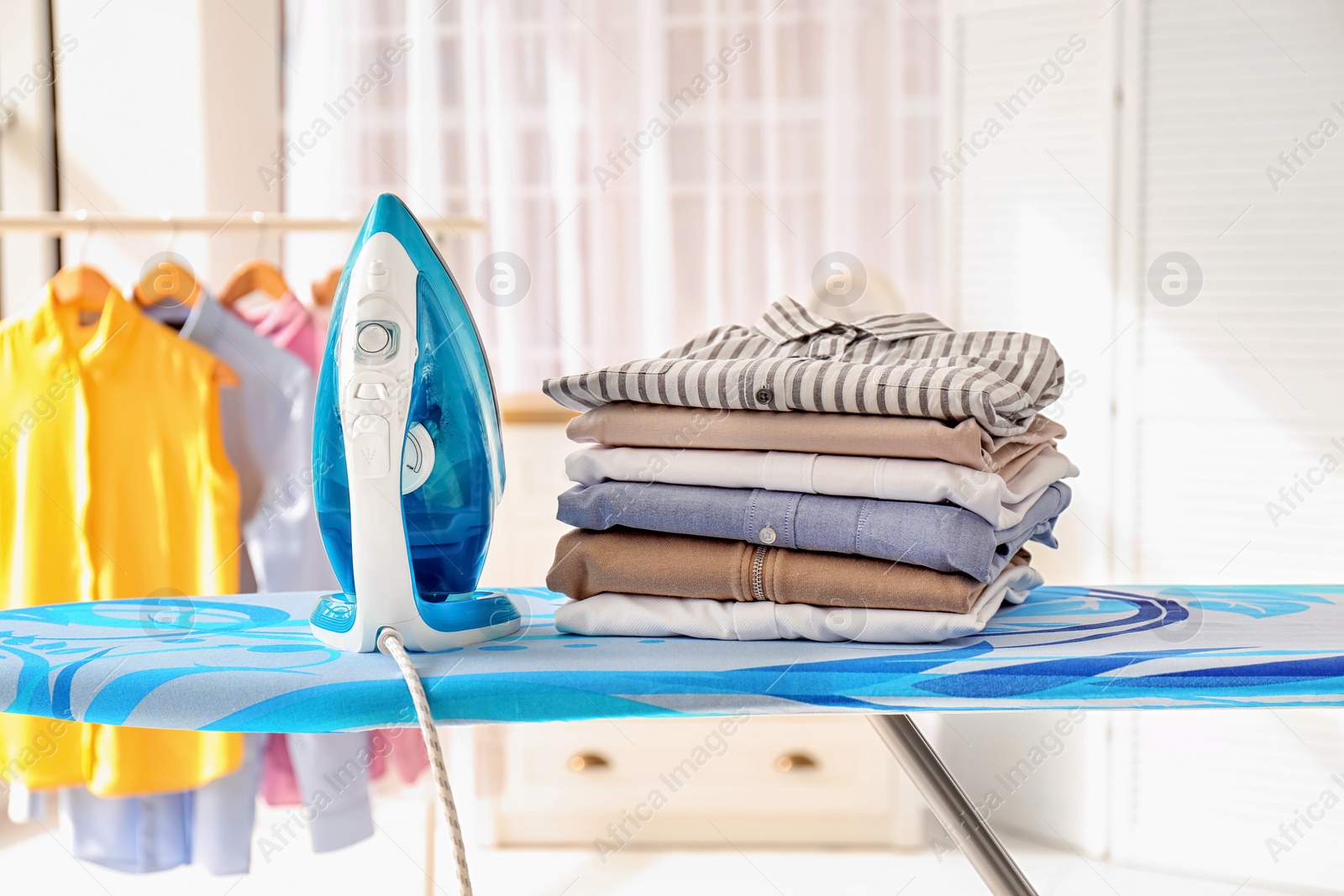 Photo of Stack of clean clothes and iron on board indoors