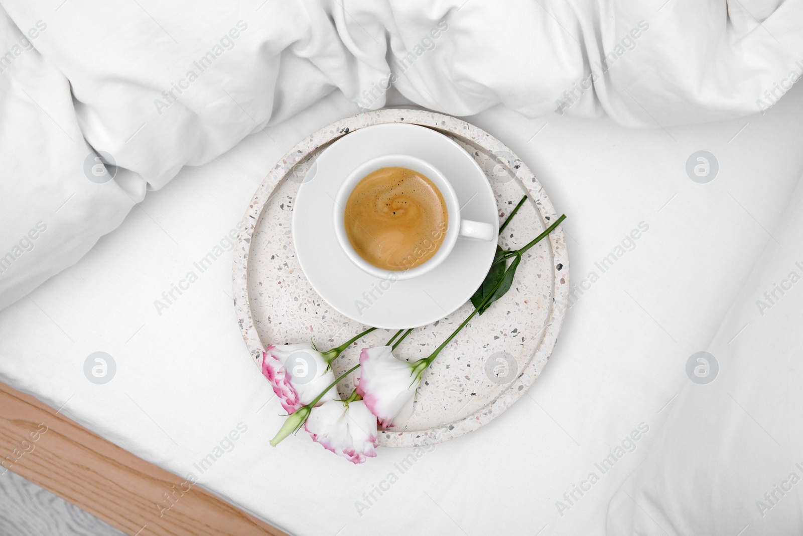 Photo of Tray with cup of coffee and flowers on white bed, top view