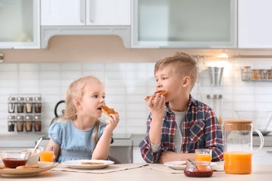 Photo of Cute little children eating tasty toasted bread with jam at table in kitchen