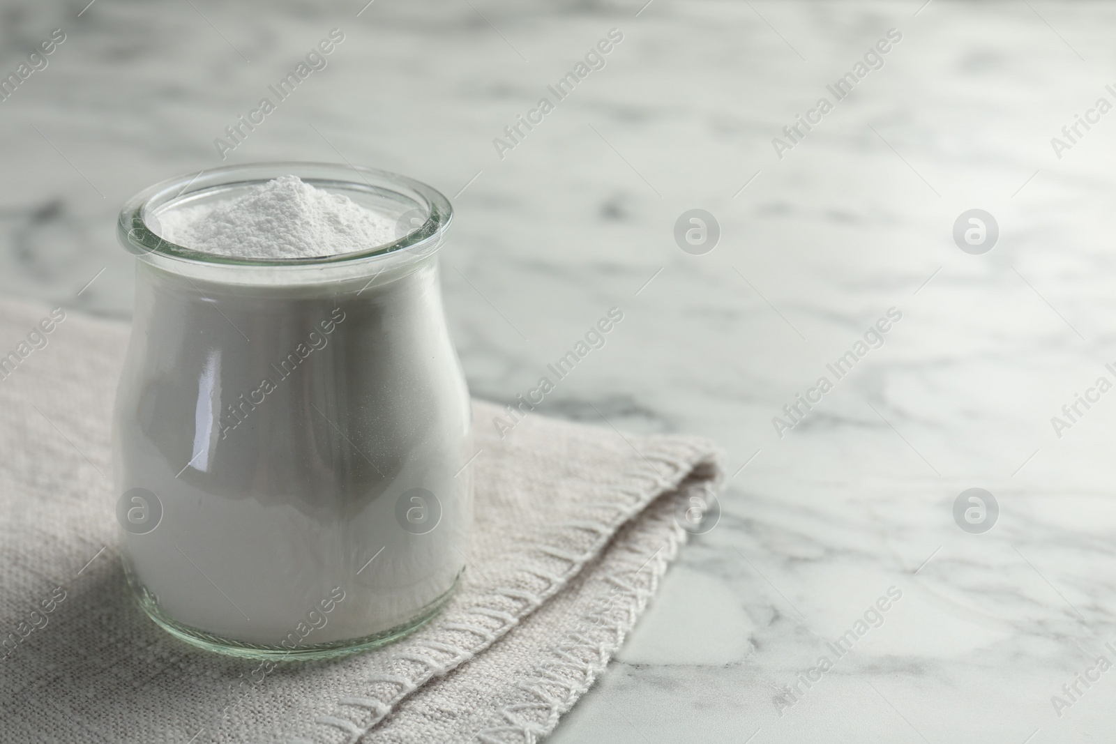 Photo of Baking powder in jar on white marble table, space for text