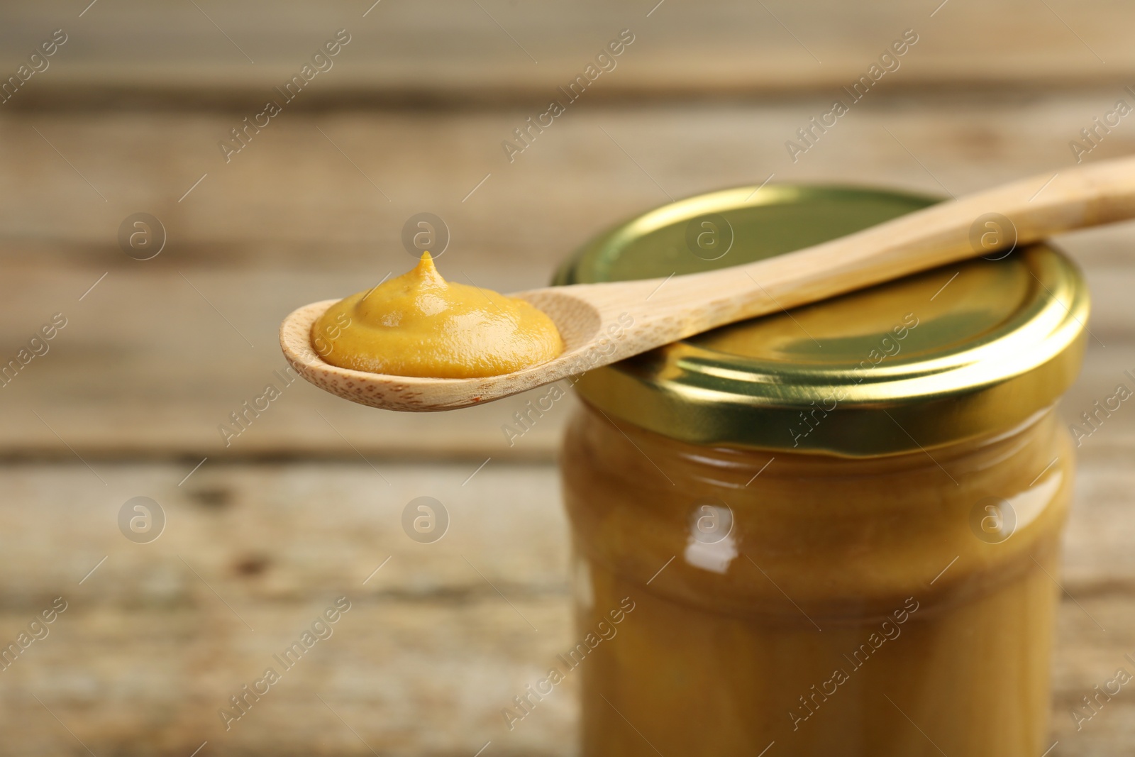 Photo of Jar and spoon with tasty mustard sauce on table, closeup