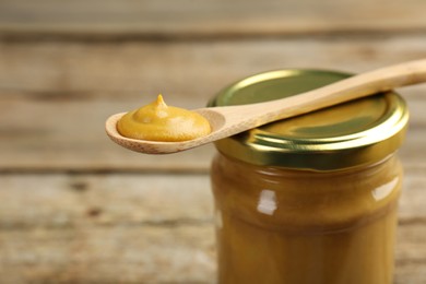 Photo of Jar and spoon with tasty mustard sauce on table, closeup