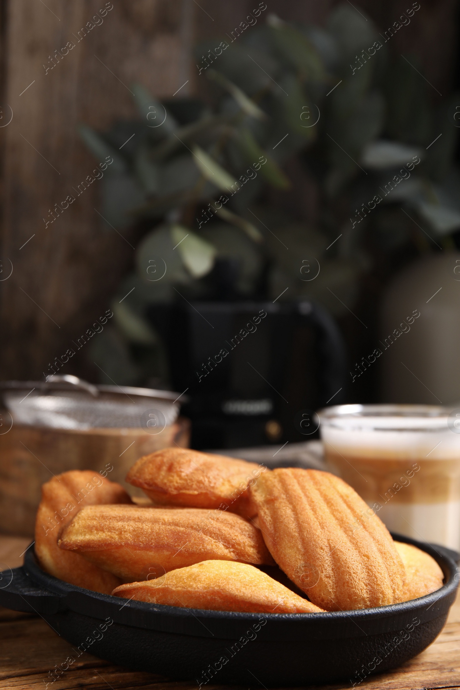 Photo of Delicious madeleine cakes in frying pan on wooden table. Space for text