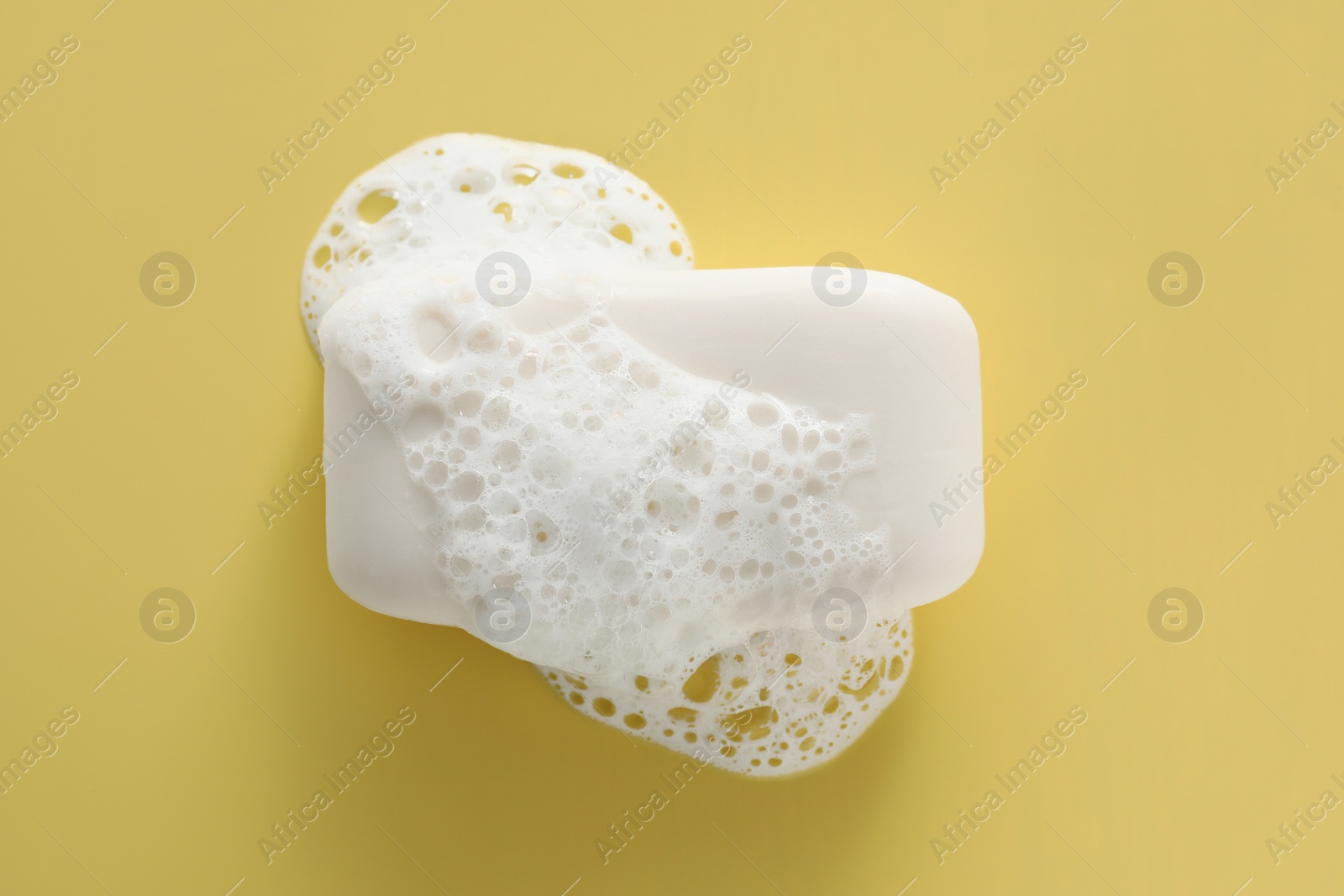 Photo of Soap bar with fluffy foam on yellow background, top view
