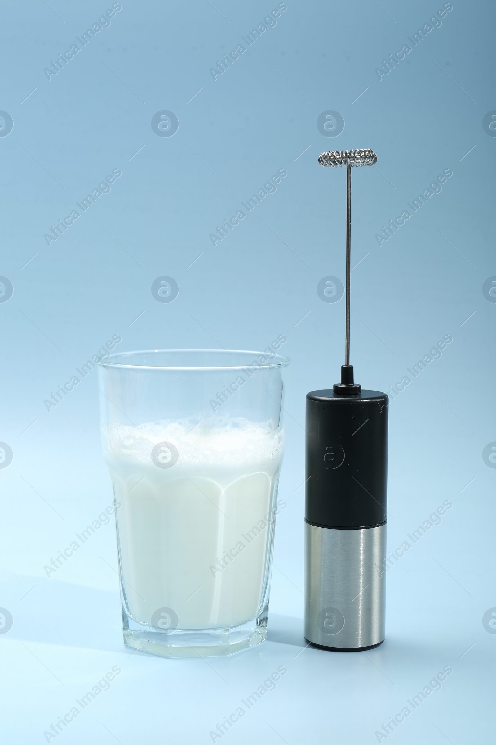 Photo of Mini mixer (milk frother) and whipped milk in glass on light blue background