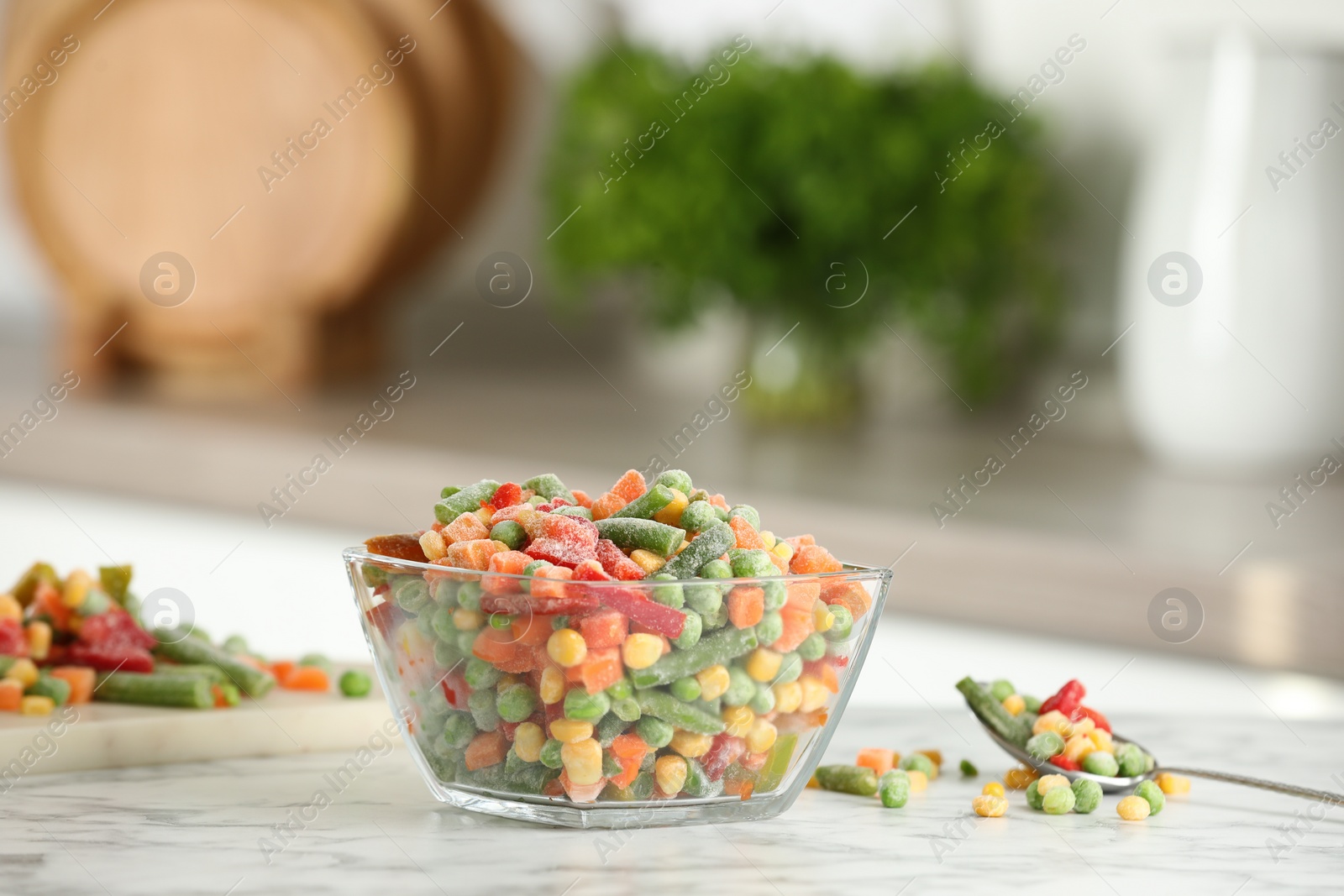 Photo of Mix of different frozen vegetables in glass bowl on white marble countertop in kitchen. Space for text