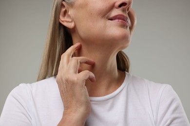 Photo of Mature woman touching her neck on grey background, low angle view