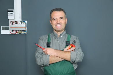 Electrician with instruments standing near fuse board on grey wall