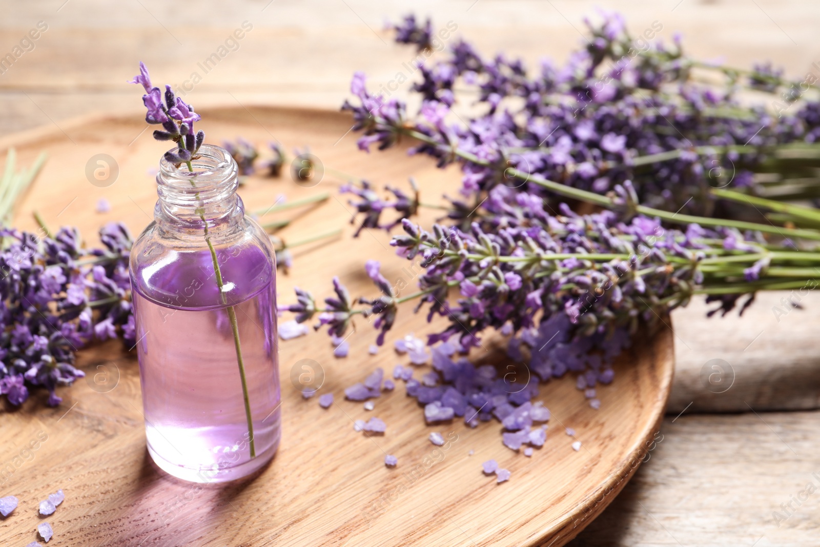 Photo of Plate with natural cosmetic oil and lavender flowers on wooden table