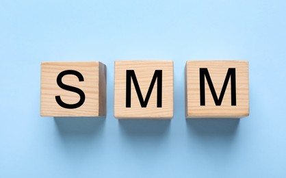 Photo of Wooden cubes with abbreviation SMM (Social media marketing) on light blue background, flat lay