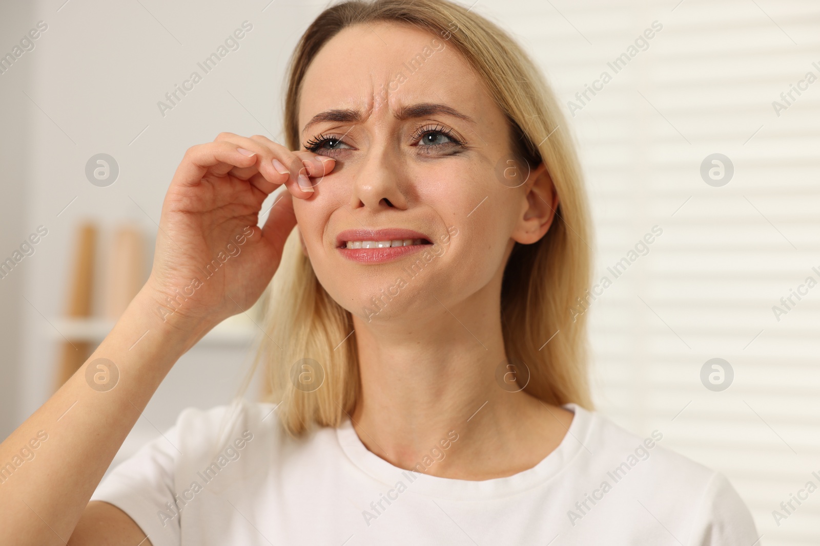 Photo of Sad woman with smeared mascara crying indoors, closeup