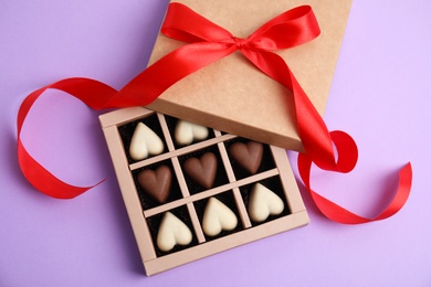 Photo of Tasty heart shaped chocolate candies on violet background, flat lay. Happy Valentine's day